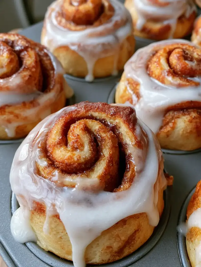 Cinnamon Roll Muffins: The Ultimate Fluffy Bakery-Style Recipe 2 A handheld smartphone photo showing a batch of Cinnamon Roll Muffins with visible tight swirls and dripping white glaze.