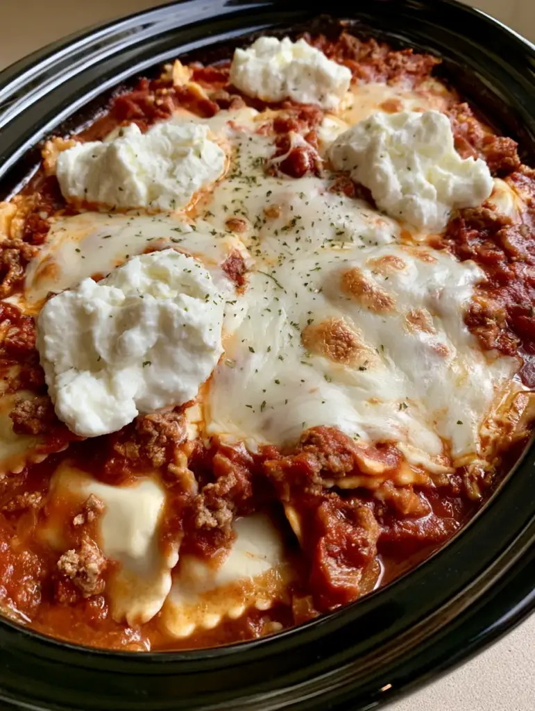 Visual layers of cheese ravioli and ricotta cheese dollops being assembled in the slow cooker.