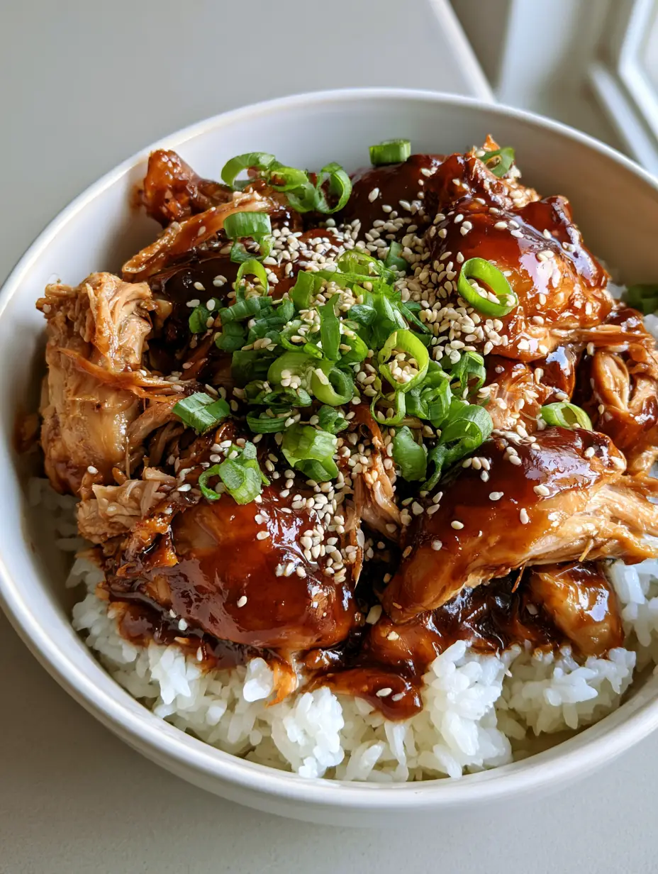 Close up of shredded slow cooker chicken thighs coated in a dark mahogany brown glaze with visible honey sheen.