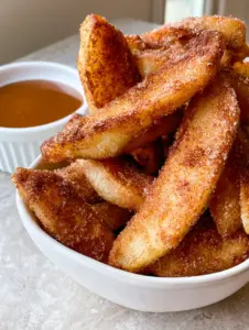 Handheld photo of Air Fryer Apple Fries in a white bowl showing the grainy cinnamon sugar texture.