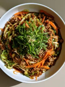 A close-up shot of sautéed shredded green cabbage and browned meat crumbles in a glossy soy-ginger sauce. (Egg Roll in a Bowl)