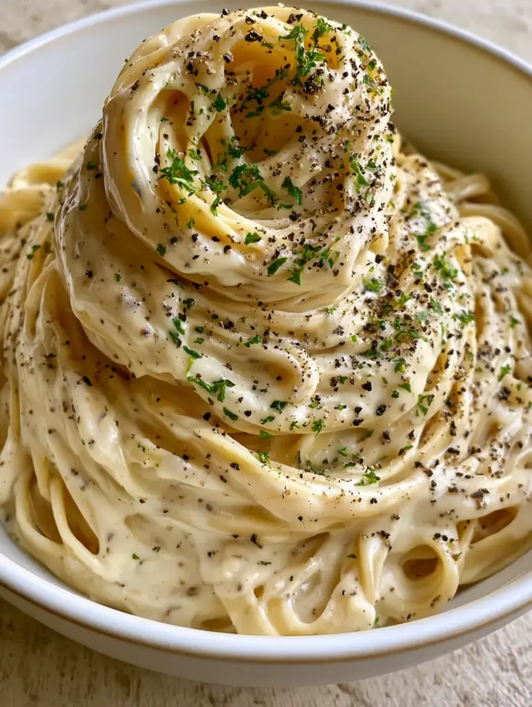 A tall swirling mound of fettuccine heavily garnished with coarse black pepper and fresh parsley.