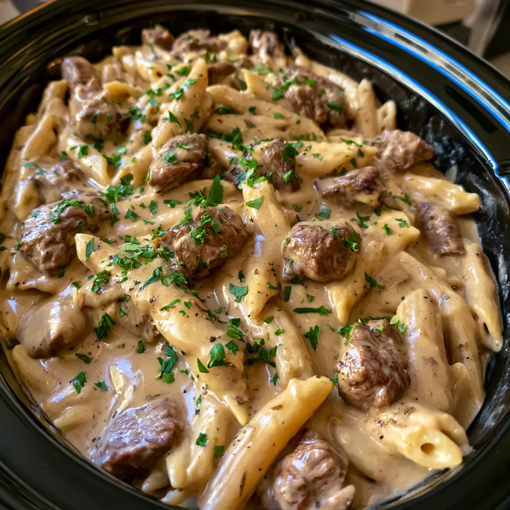 Slow Cooker Garlic Beef Pasta (Creamy & Tender) 1 Close-up of penne pasta coated in thick pale brown garlic cream sauce with beef and black pepper.