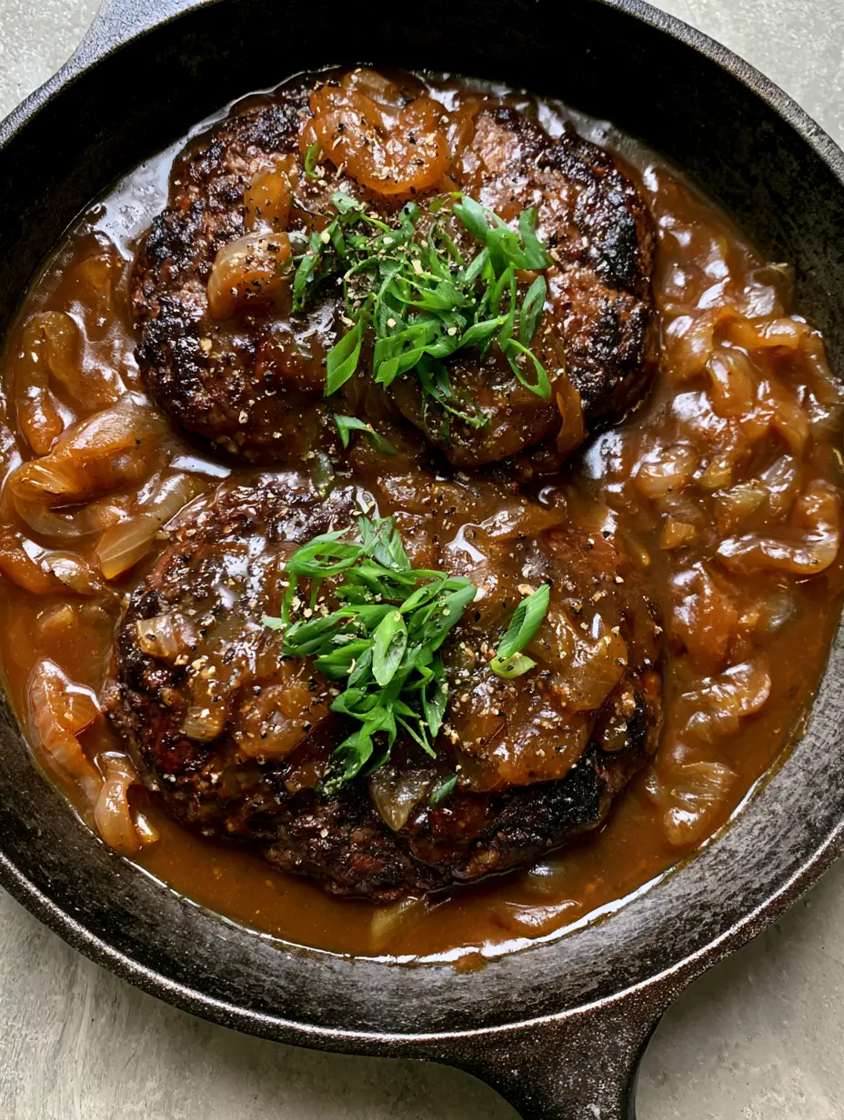 Close-up of thick oval hamburger steaks seared to a dark brown crust in a seasoned skillet. (Hamburger Steak with Brown Gravy)